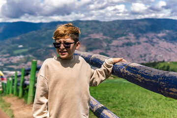 Colombian boy shielding his eyes from sunlight while standing by a scenic overlook above a mountain...
