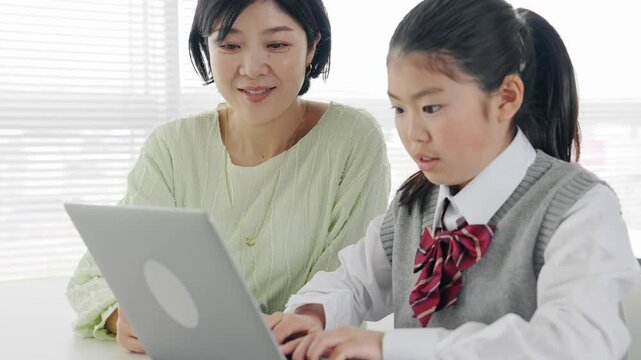 教室で女性教員からパソコンを教わる女の子