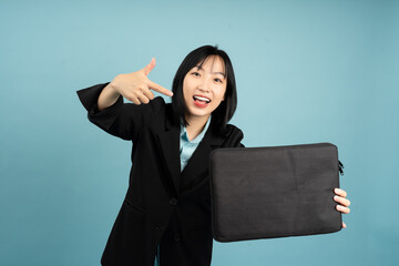 Cheerful Asian woman in professional attire showcasing a black bag against a light blue backdrop,...