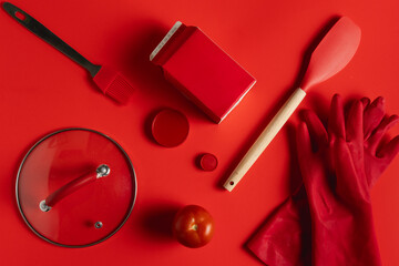 Red kitchen utensils, tomato and gloves on red background
