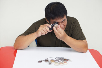 A Thai man carefully inspects sacred amulet using a magnifying glass, showing passion and faith....