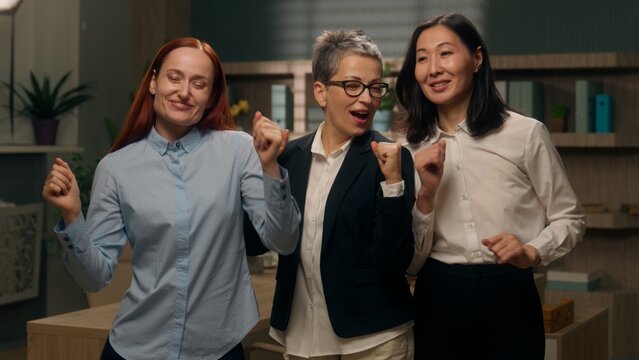 Happy multicultural team women dancing celebrate victory achievement financial deal success business company businesswomen businesspeople win multiethnic females employers coworkers colleagues office
