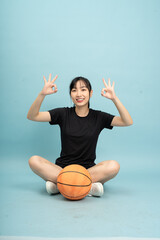Girl with basketball shows victory signs while sitting on the floor against a light blue background
