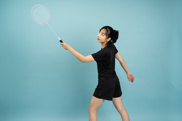 Young Asian woman practicing badminton with a racket against a solid blue background during an...