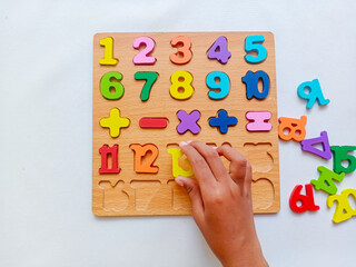 Asian child hand playing colorful wooden number puzzle board with math symbols for early learning