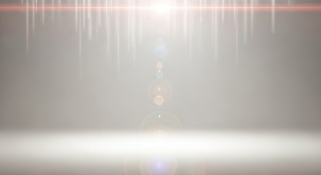 A bright white light shines down in an empty room with a gray background creating a lens flare effect