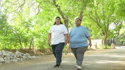 Obesity Concept- Indian couple walking together at summer park to loose weight. Plus size friends Fitness and healthy lifestyle. Fat man and woman outdoor. 4k - Powered by Adobe