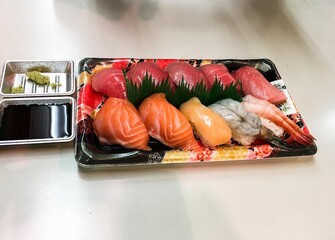 close up of takeaway assorted raw sashimi sushi, including salmon, tuna, octopus, prawns and clam, on a plastic box with soy sauce and wasabi on the side