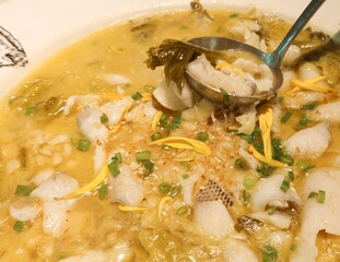 close up of Chinese Sichuan spicy and sour Boiled Fish with Pickled Cabbage with a spoon holding a slice of fish