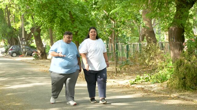 Overweight Indian Asian couple walking together in a summer park for fitness, weight loss, and healthy lifestyle motivation. Obese man and woman doing outdoor exercise for wellness, body positivity, 
