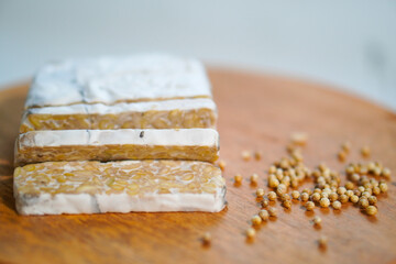 Tempeh that has been cut into pieces on a wooden chopping board with added coriander as a...