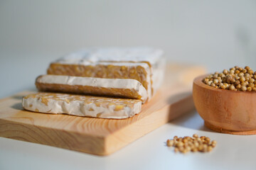 Tempeh that has been cut into pieces on a wooden chopping board with added coriander as a complement.