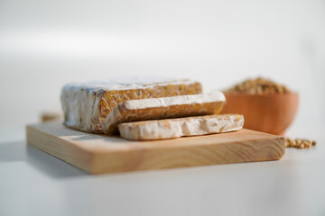 Tempeh that has been cut into pieces on a wooden chopping board with added coriander as a...