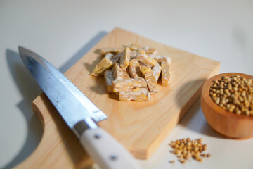 Tempeh that has been cut into small pieces on a wooden chopping board, complete with a knife and a...