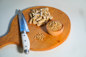 Tempeh that has been cut into small pieces on a wooden chopping board, complete with a knife and a...
