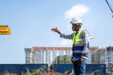 African American Engineer or Supervisor Directing at Construction Site, Male Worker with Hard Hat...