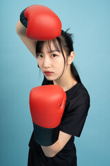 Young Asian woman in boxing stance with red gloves prepares for a match against a solid light blue...