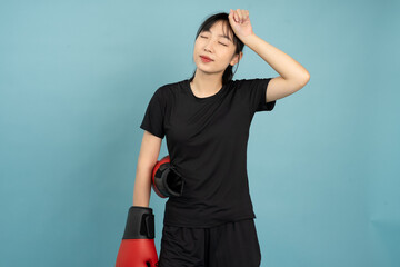 Woman relaxing after boxing workout in a studio with a plain blue background, showcasing physical...