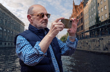Mature Man Taking Photos with Smartphone Near Urban Canal Landscape