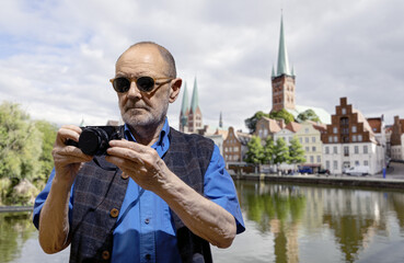 Man Photographing Historic Architecture Near a Scenic River on a Sunny Day