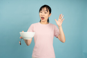 Woman expressing surprise while holding a bowl in a simple setting with a light blue background
