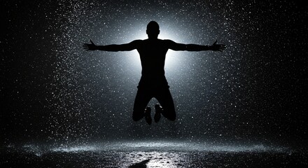 Naklejka premium A powerful silhouette of a man jumping high with outstretched arms amidst a dramatic splash of water or rain.