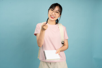 A young Asian student in casual attire is holding a notebook while gazing thoughtfully into the...
