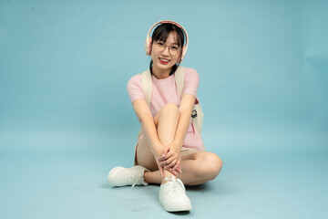 Young woman with headphones sitting on a blue backdrop while smiling and showcasing a casual and...