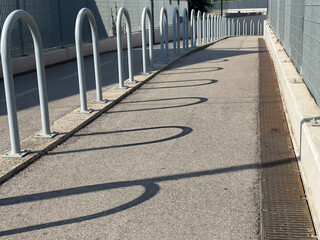 Curved pathway with metal barriers casting shadows in urban setting