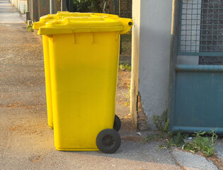 Yellow trash bins on street in sunlight near fenced area