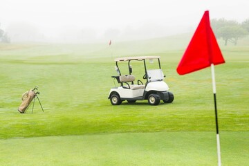 White two-seater golf cart is sitting on misty fairway in vector illustration with bag, red flag
