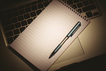Vector art showing notepad lying across laptop keyboard palm rest with ballpoint pen casting shadow