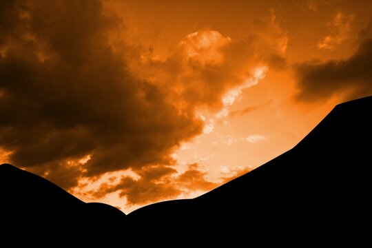 Fototapeta Silhouetted hill ridge is stretching across flat vector design with orange sky and clouds