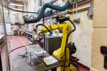Yellow industrial robotic arm is clamping metal plate inside safety cage in flat design lab