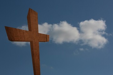 Rough-hewn wooden cross standing left of center against deep blue sky with drifting white clouds