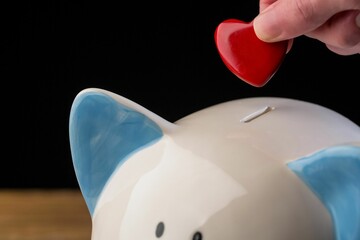 Hand putting red heart coin in piggy bank