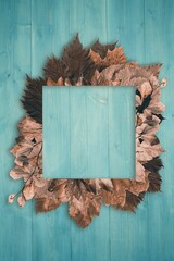Obraz premium Flat square turquoise frame is resting on painted wood surface surrounded by brown leaves