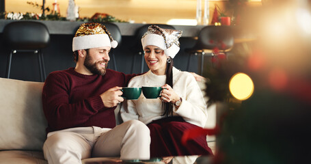 Christmas, cheers and couple with coffee in home for festive morning with santa hat for celebration. Happy, love and man with woman on sofa for relax, bonding and drinking eggnog for xmas together.