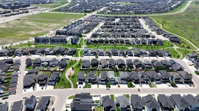 Residential neighborhood with many houses and a few cars. The houses are mostly white and the street is lined with trees