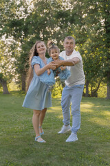 Fototapeta premium Young and happy parents playing with their little daughter in the park on a sunny summer day. The concept of family, vacation with a child, and raising children