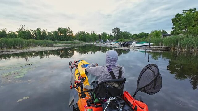 Kayak fishing game, angler at weedy lake pond, fishing pdl kayak during tournament. Sport and bass fishing activity in the morning on pedaling fishing kayak. Water hobby and active lifestyle.