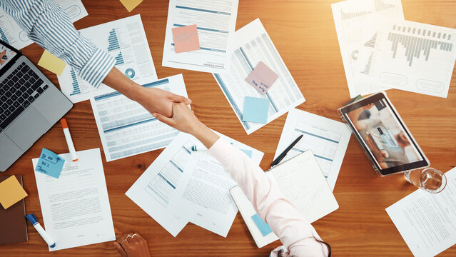 Above, business people and handshake in meeting with graphs, data analysis and feedback. Shaking hands, collaboration and documents for project, research and tech for chart review with paperwork
