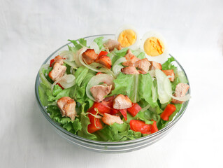 A cesar salad bowl filled with lettuce, tomatoes, egg and chicken. The salad is served in a clear glass bowl