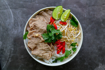 A Bowl Pho Bo traditional Soup with beef, rice noodles, ginger, lime, chili pepper in bowl. Close...