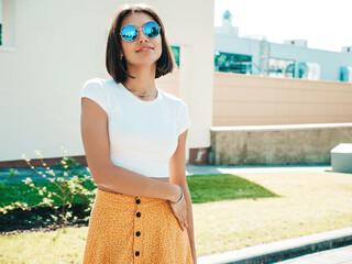 Portrait of beautiful smiling brunette model dressed in summer hipster  clothes. Trendy female posing in the street near white wall. Funny and positive woman having fun