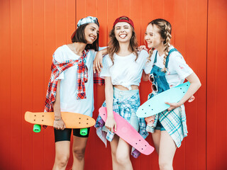 Three young smiling beautiful female with colorful penny skateboards. Women in summer hipster clothes posing in the street background. Positive models having fun and going crazy