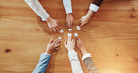 Business people, hands and meeting with jigsaw puzzle for team building on wooden table above. Top...