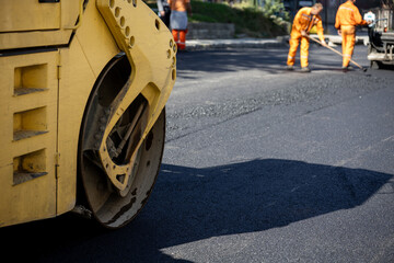 Road maintenance workers using a steamroller on a freshly paved street during daylight hours