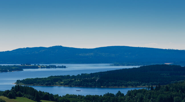 Ship float on dam Lipno with forest layer and blue sky. Czech landscape, vacation background