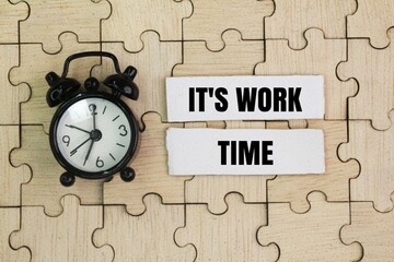 Alarm clock, paper and the words it's work time with a puzzle background. a time period when you...